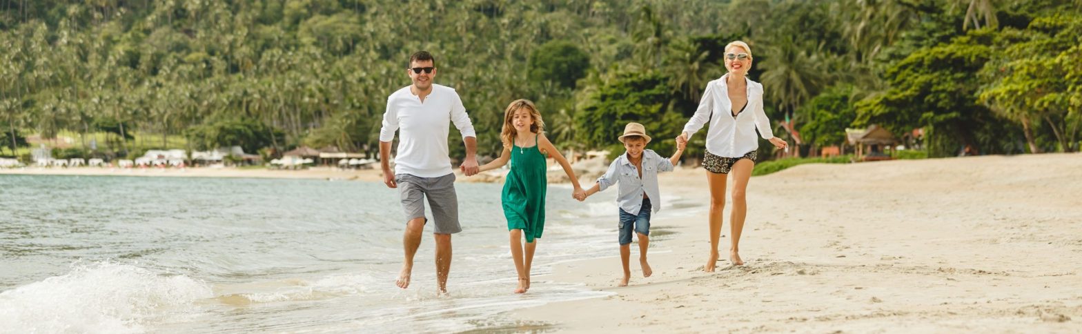 Imagen de frente de una familia con dos hijos dando un paseo por una playa cristalina