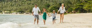Imagen de frente de una familia con dos hijos dando un paseo por una playa cristalina